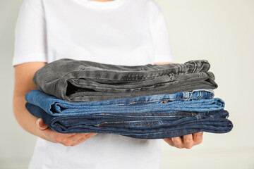 Woman with stack of different stylish jeans near light wall indoors, closeup