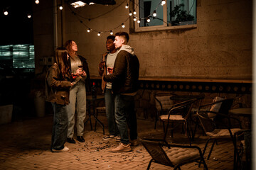 Friends enjoy an evening gathering outdoors under fairy lights in a lively atmosphere
