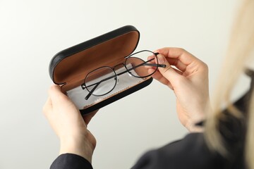 Woman holding case with stylish glasses and cleaning cloth on light background, closeup