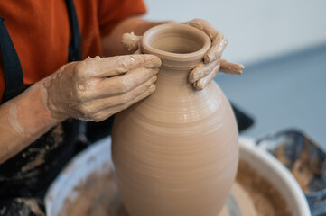 Close-up of a potter's hands making a ceramic vase on a potter's wheel. 
