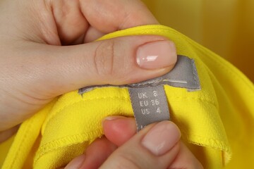 Woman holding clothing label of yellow garment, closeup