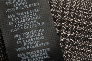 Clothing label in different languages on black garment, closeup