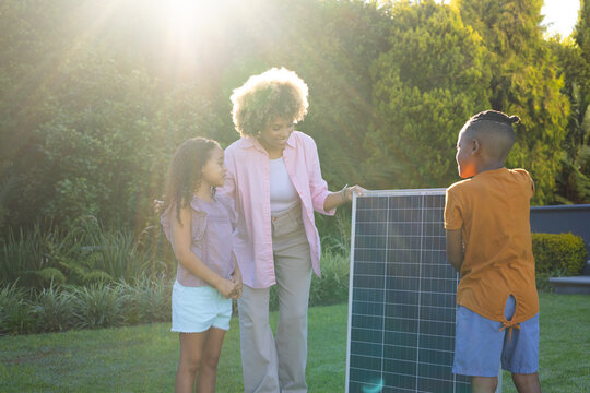 African American family holding solar panel upright in backyard garden, with sunlit shrubs