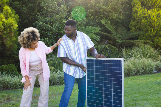 Diverse couple installing solar panel in residential backyard garden, embracing green energy - Powered by Adobe