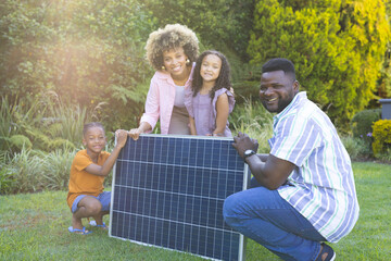 Smiling Diverse family kneeling and crouching on backyard lawn, with large solar panel installation