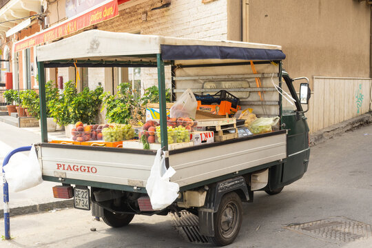 Sicily, Italy - August 17, 2024: Parked Piaggio Ape selling peaches, grapes and other fresh produce in a city street market