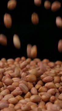 Raw whole dried peanut kernels pour, close-up, vertical slow motion