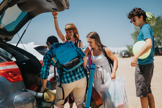 A group of friends are organizing and packing their car with essential items for a fun summer beach trip. They are smiling, laughing, and appear to enjoy the sunny day and each other's company.
