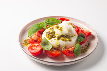Burrata cheese caprese salad with cherry tomatoes, olive oil, pesto and seasoning. Fresh food concept