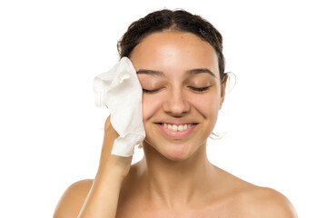 A smiling young woman cleans makeup from her face with wet wipes on a white background