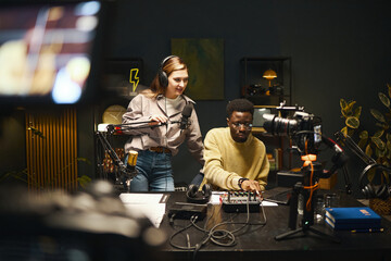 Young people using mixing console and microphone to record podcast together in studio