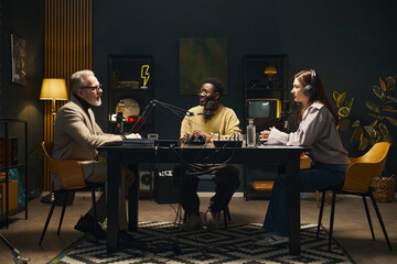 Young people sitting at table with microphones and talking to man during online podcast
