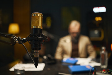 Close-up of professional microphone for podcast in studio with man reading script in background