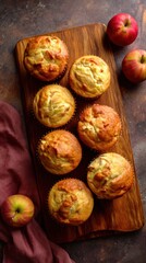 Golden apple muffins displayed on a wooden board with fresh apples and a burgundy cloth creating a warm rustic food photography scene