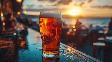 Pint of beer sits on a bar with a sunset and ocean backdrop.