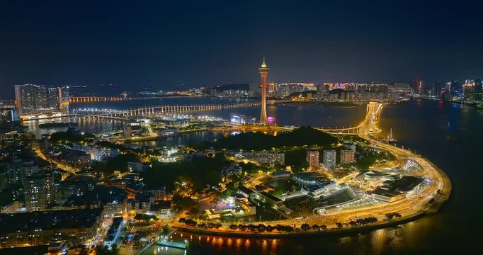 Aerial shot of Macau cityscape skyline illuminated at night with bridge and waterfront buildings. Travel tourism and entertainment background in Asia.