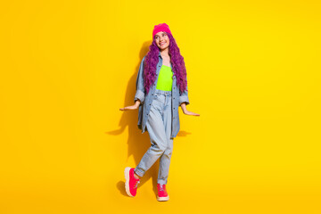 Stylish young woman with vibrant pink hair and denim outfit posing playfully against a bright yellow background