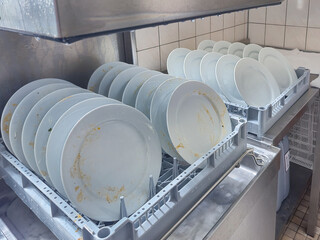 many dish or white plate arranged on basket for cleaning by automatic dishwasher machine in kitchen room restaurant