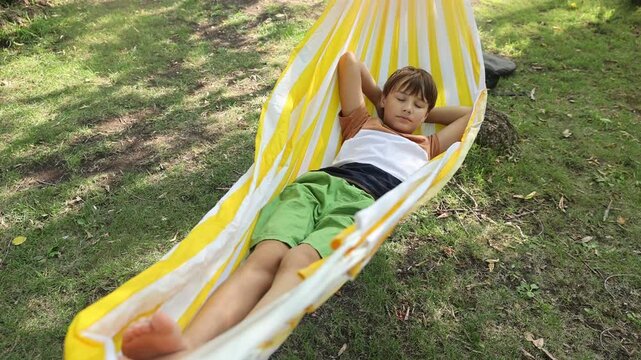 A portrait laughing preteen boy lies in a hammock having fun summer outdoor. Generation Z. Happy childhood.

