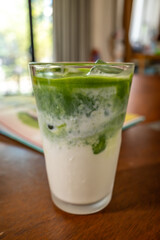 Ice milk matcha green tea in clear glass, home made Japanese style, on brown wooden table in house