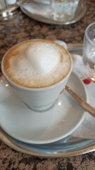 Cup of cappuccino with thick milk foam served on a saucer in a cozy cafe setting. The image evokes a relaxing coffee break and European cafe culture experience