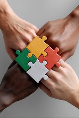 Multiple hands from various ethnic backgrounds fit puzzle parts together, creating a colorful image - international teamwork global bonding