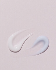 Two cosmetic cream textures — white and light blue — smeared on soft pink background.