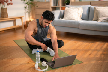 Fit young man resting on yoga mat after home workout