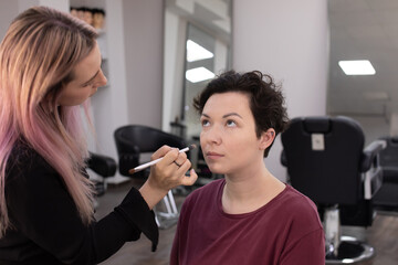 Professional beautician applying makeup on beautiful young woman's face. Professional make up studio work with gorgeous female model.