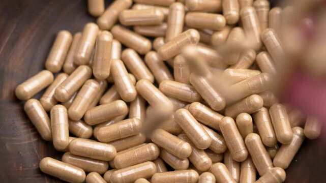 Supplement capsules with nutrient extracts falling from hand into wooden bowl in slow motion