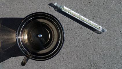 A broken medical mercury thermometer and a drop of mercury in a cup of water.