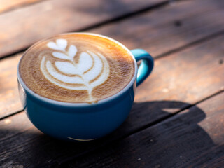 A cup of cappuccino coffee, with a blue cup placed on a black wooden table. Beautiful latte art with leaf shape.