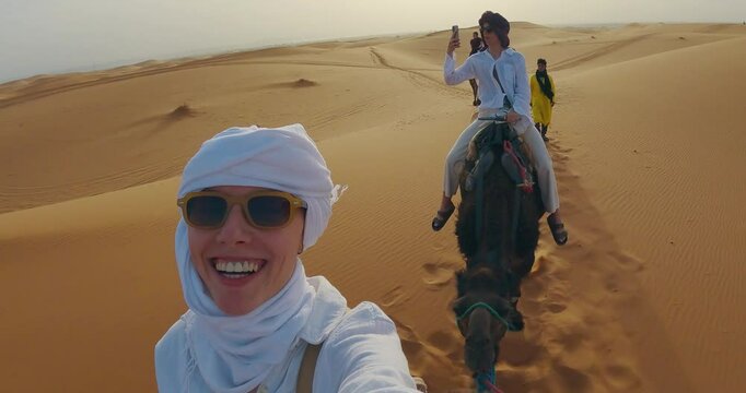 Group of individuals rides camels in a desert environment during a safari tour