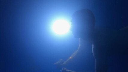 Man swimming underwater in pool at night illuminated by bright led light