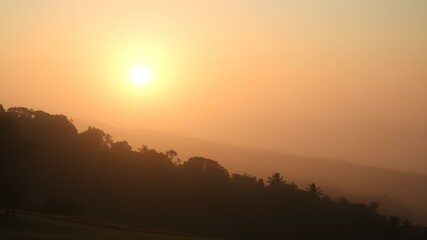 Golden Hour's Embrace: The radiant sun casts a warm, ethereal glow over a serene, silhouetted landscape, hinting at a moment of peaceful transition. 