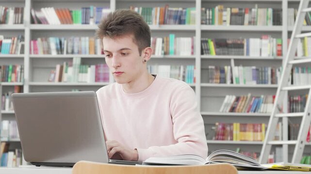 Focused young male student immersed in laptop study at college library