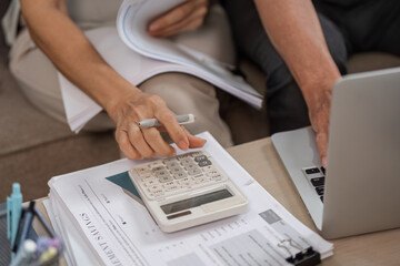 Elderly Couple Managing Family Finances with Calculator and Laptop at Home