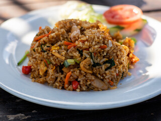 Fried rice on a white plate, with a cup of coffee in the background. Traditional Indonesian cuisine. Asian food.