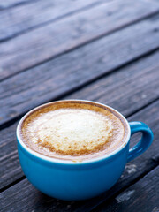 A cup of cappuccino coffee, with a blue cup placed on a black wooden table.