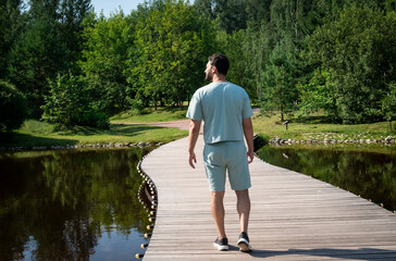 Back view on handsome man walking on the bridge in the park in wonderful summer day. Leisure time and travel concept