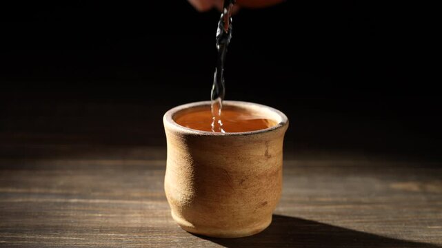 Japanese sake from a bottle being poured into ceramic cup on a wooden table, close up