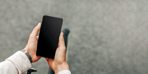 A guy is standing on the street, holding his smartphone while surrounded by a vibrant urban atmosphere. Dressed casually, he embodies the millennial lifestyle.
