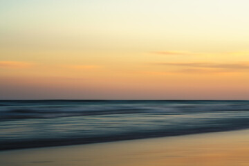 Abstract sunset scene with blurred waves and soft, warm hues on the horizon.