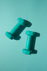 Sport or workout concept flat lay with blue dumbbells on the blue teal background. 