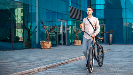 Modern worker and coffee break. Guy with bag and cup of coffee goes with bike near office building