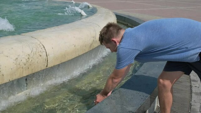 Man suffering from heat wave in the city and cooling off in city fountain. Exhausted tired overheated man tourist. Sunstroke at summer hot weather