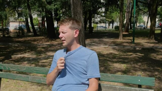 Man suffering from heat wave, guy with heatstroke. Caucasian male presses bottle of water to face to cool off. Exhausted tired overheated man. Sunstroke at summer hot weather