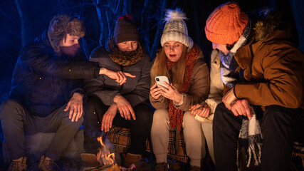 Obraz premium Friends sitting around a campfire in the woods on a winter evening