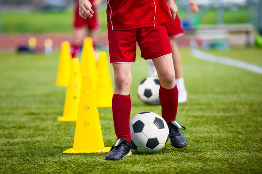 Children in red soccer uniforms practicing dribbling skills around yellow cones on a grassy field during a soccer training session