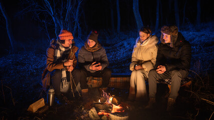 Friends sitting around a campfire in the woods on a winter evening